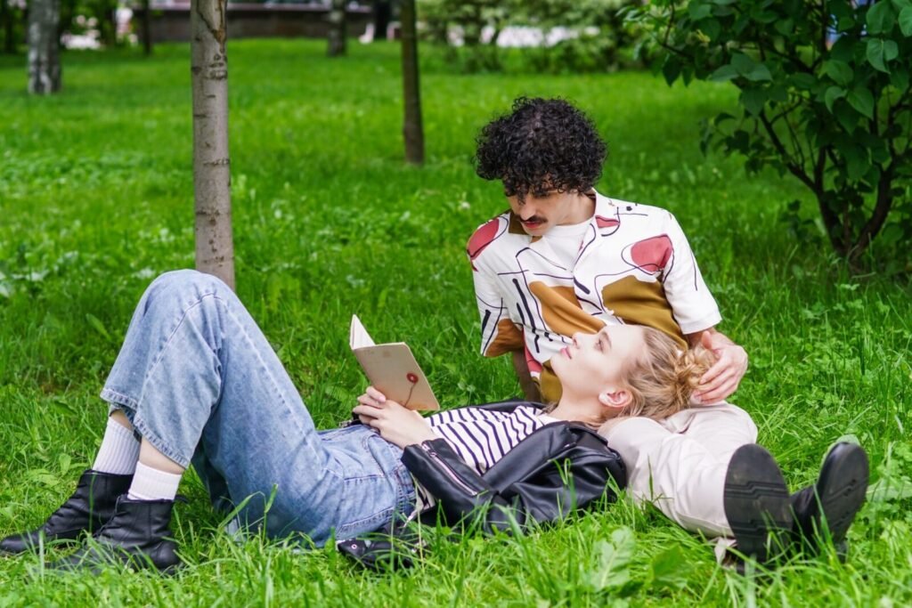 A couple enjoys a peaceful moment outdoors, lying on grass and reading together.