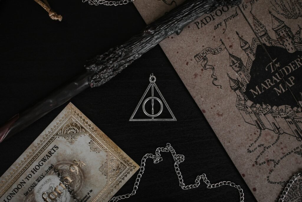 A metal Deathly Hallows pendant, a wand, and a map on a black surface